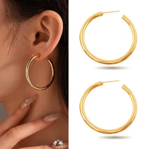 Detailed view of large gold-tone stainless steel hoop earrings worn and on white background.