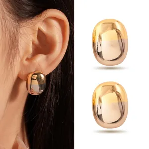 Detail view of gold stainless steel oval stud earrings on model's ear and flat lay.