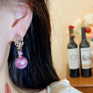 Close-up of elegant gold leaf earrings with purple crystals and large dangling pearls.