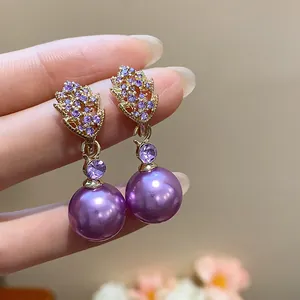 Detailed close-up of gold-plated leaf earrings with purple stones and pearls.