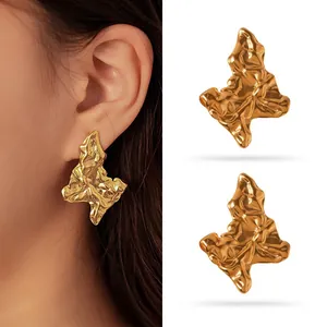Close-up of gold irregular crumpled metal stud earrings on a model and white background.
