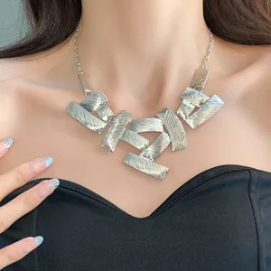 Close-up of a silver geometric necklace with textured metal plates shown on a model.