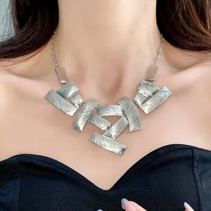 Close-up of a chunky silver-toned necklace with textured geometric square plates.