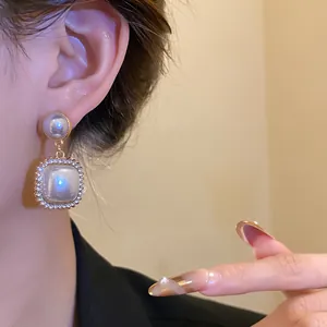 Dettaglio di eleganti orecchini pendenti con perle quadrate in stile palazzo vintage e strass