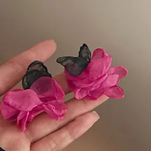 Macro view of pink fabric flower stud earrings with delicate black mesh butterfly wings