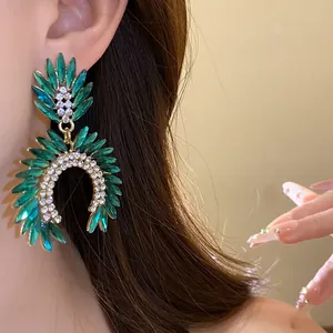 Close-up of elegant green crystal drop earrings with sparkling rhinestones on ear.