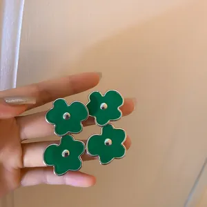 Close-up view of retro green flower stud earrings with enamel finish and silver needles.