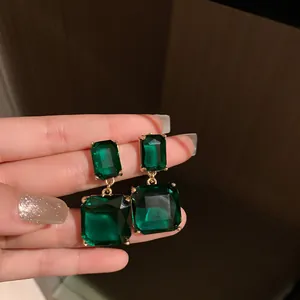 Close-up of elegant emerald green square-cut drop earrings with a vintage gold setting