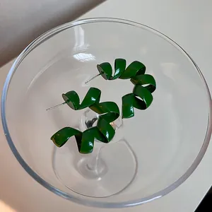 Detail view of retro glossy dark green spiral ribbon earrings in a crystal cocktail glass