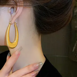 Primo piano di grandi orecchini a cerchio geometrici ovali dorati indossati da una modella