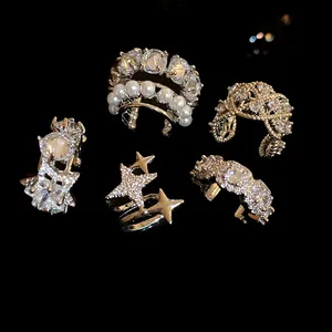 Vista de detalle de cinco ear cuffs brillantes con circonitas y perlas sobre negro.