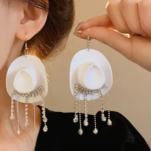 Dettaglio di orecchini bianchi a forma di cappello da cowboy con nappe di strass lucidi.