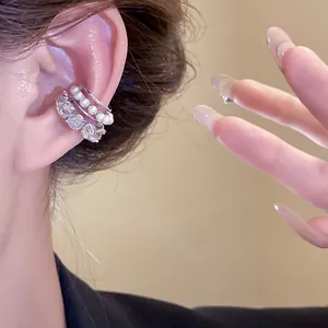 Detalle de un ear cuff plateado de varias capas con circonitas y perlas en la oreja.
