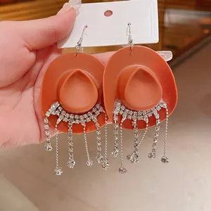 Dettaglio di orecchini creativi a forma di cappello da cowboy arancione con strass