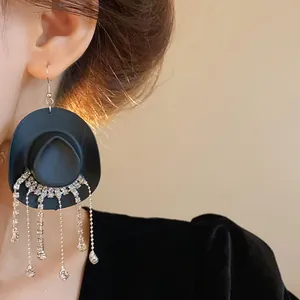 Primo piano di creativi orecchini a cappello da cowboy nero con lunghe nappine di strass