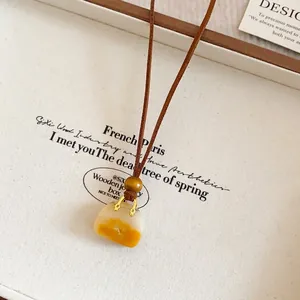 Close-up of a vintage leather cord necklace with a yellow handbag-shaped resin pendant.