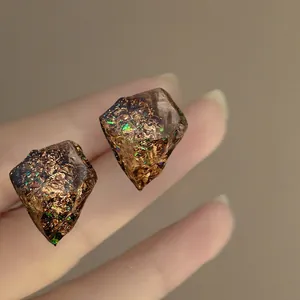 Detailed macro view of irregular resin stud earrings with gold foil and iridescent glitter