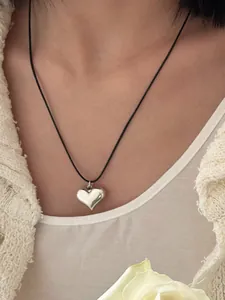 Macro detail view of a polished silver heart pendant on a minimalist black cord