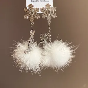 Dettaglio di orecchini a pompon bianchi con fiocchi di neve d'argento e ciondoli cervo.