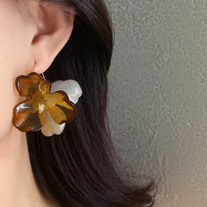 Gros plan d'une grande boucle d'oreille fleur en acrylique ambre et blanc portée