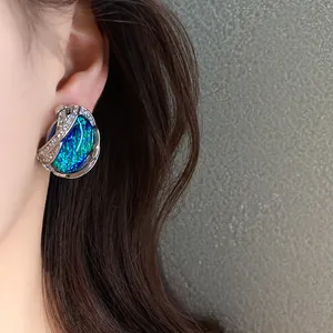 Dettaglio dell'orecchino in resina iridescente blu-verde con bordo di strass lucenti.