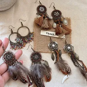 Set di orecchini etnici bohémien con nappe di cotone, piume e perline su tela di sacco