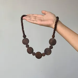 Retro style dark brown wooden bead necklace featuring large round flat pendants displayed by hand