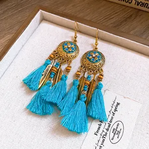 Dettaglio di orecchini etnici con smalto blu, piume dorate e nappe blu brillante