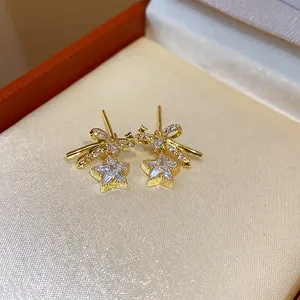 Primer plano de pendientes de lazo y estrella dorados con circonitas en estuche