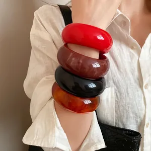 Detailed view of stacked colorful retro chunky resin bangles worn on arm with a linen shirt