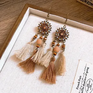 Dettaglio di orecchini etnici in resina con nappe di cotone marrone e beige su ganci.