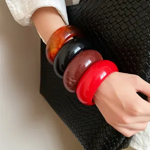 Close-up of colorful round resin bangles on wrist with a black woven bag accessory