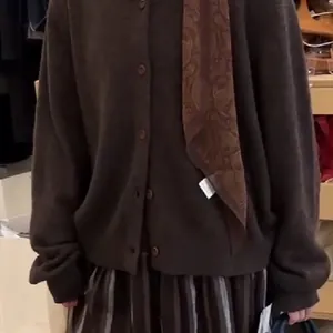 Detail einer braunen Paisley-Stoffschal-Halskette kombiniert mit einer Strickjacke.