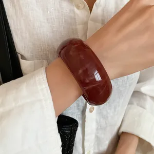 Macro view of a marbled dark red resin bangle bracelet worn on a white linen sleeve