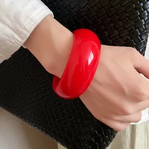 Close-up of a vibrant red chunky retro bangle worn on a wrist against a dark bag.