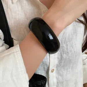 Detailed view of a wide glossy black chunky resin bangle bracelet styled with a white shirt.