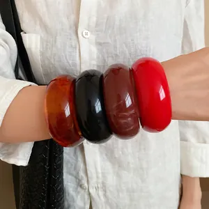 Close-up view of four colorful chunky acrylic resin bangles worn on a model arm for fashion