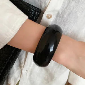 Close-up of a stylish wide glossy black chunky bangle bracelet worn on a female wrist