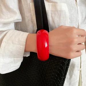 Vibrant red chunky resin bangle on wrist styled with white linen shirt and woven bag