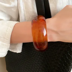 Close-up of a vintage marbled amber resin chunky bangle bracelet worn on the wrist