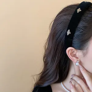 Detailed view of a stylish black velvet headband with elegant gold bee charms on a model.