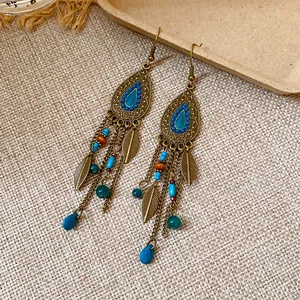 Dettaglio di orecchini bohémien a goccia con foglie di bronzo e perline blu.