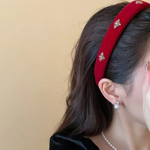 Close-up side view of a red velvet headband with golden bee ornaments on a model