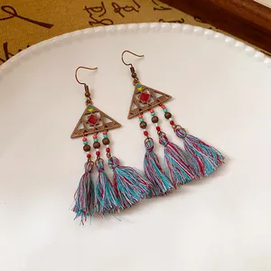 Dettaglio ravvicinato di orecchini boho con nappe, triangolo in bronzo e fili colorati
