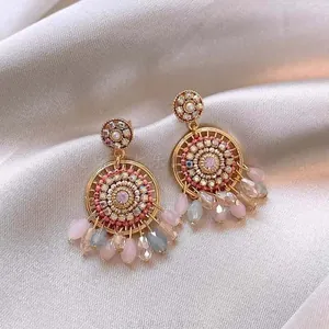 Close-up of bohemian tassel earrings with pink crystals and beads on silk background