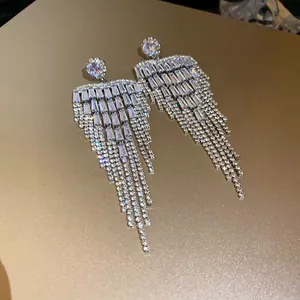 Close-up of sparkling long zircon tassel earrings on reflective gold surface.