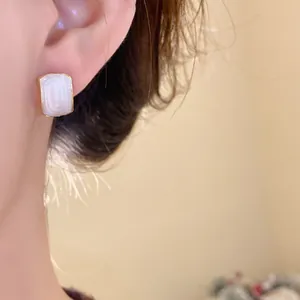 Primer plano detallado de pendientes retro franceses con marco dorado y esmalte blanco perla
