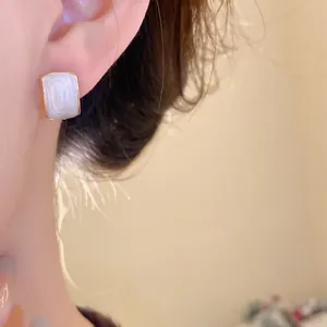 Primer plano de un elegante pendiente de botón rectangular vintage con esmalte blanco