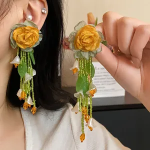 Detail of forest style earrings featuring yellow fabric roses and green beaded tassels