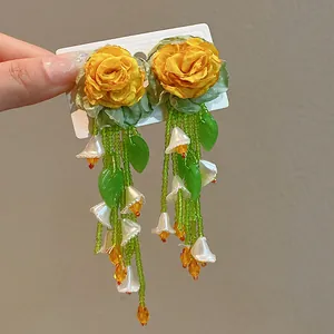 Close-up detail of yellow fabric rose earrings featuring long green beaded tassels